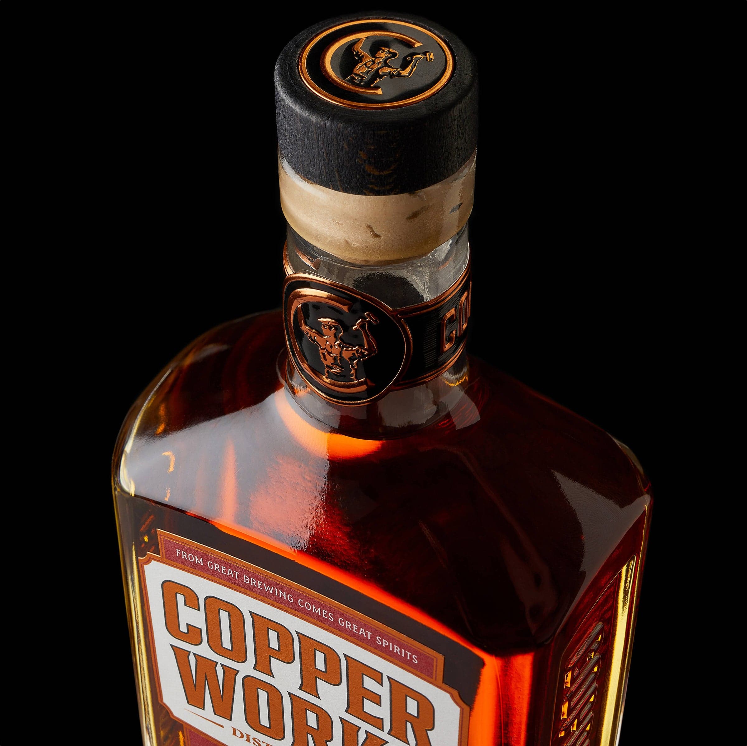 Close-up of a Copperworks bottle neck with its copper wax seal and amber whiskey against black