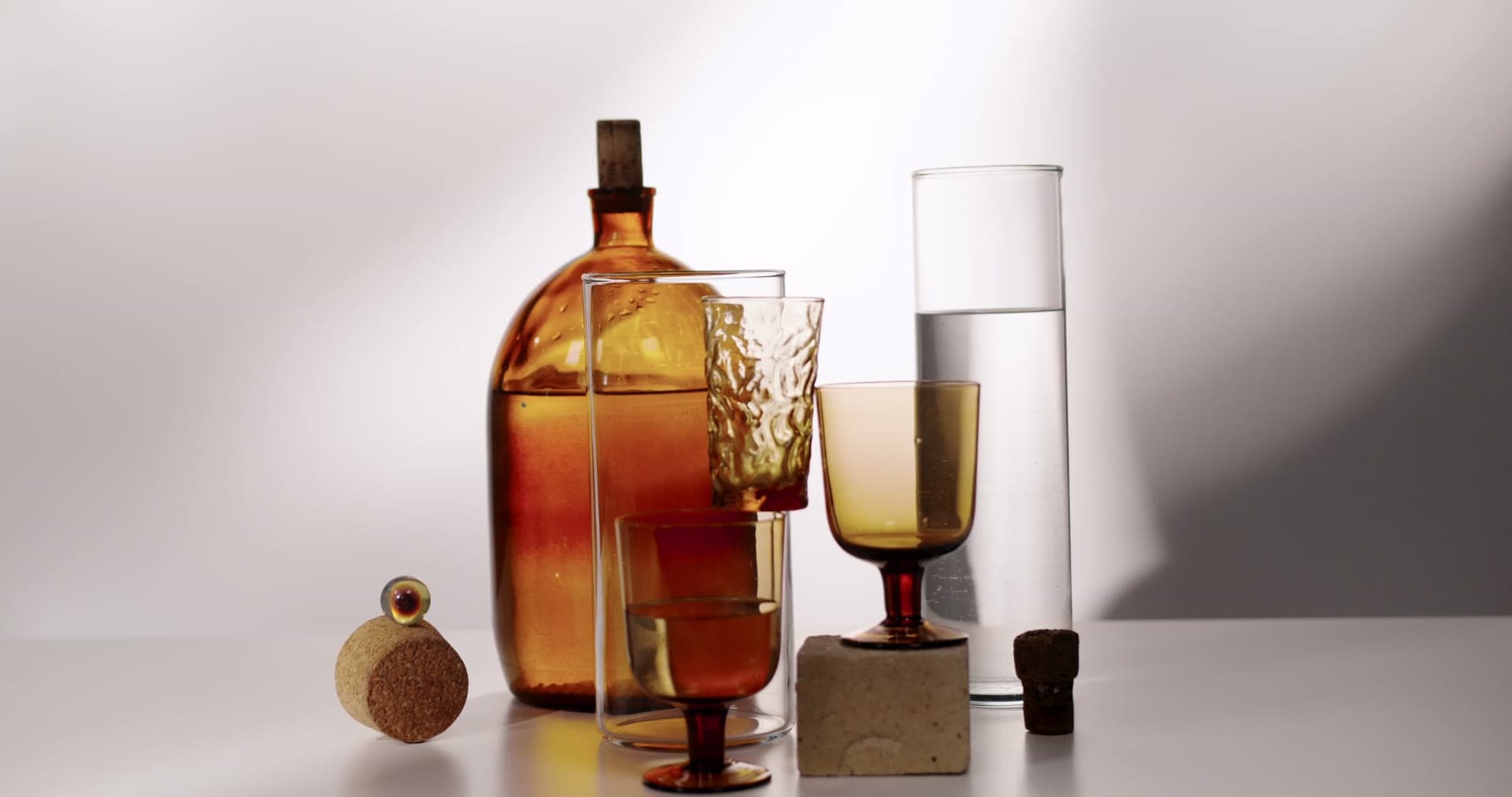 Amber spirit glowing in glasses beside a bottle, lit against a pale studio ground