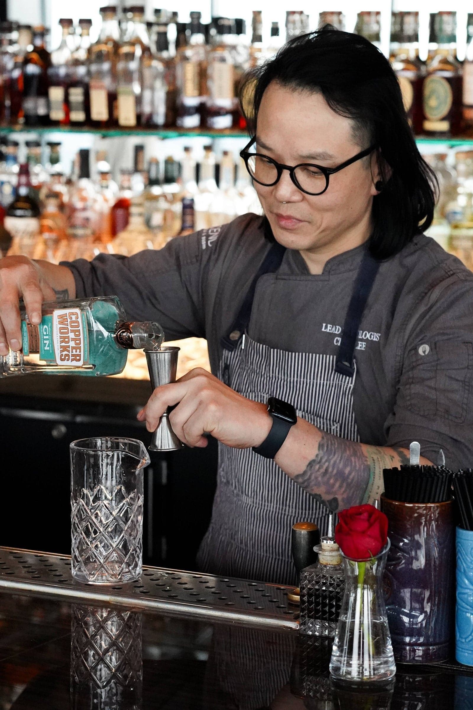 Chaz Lee pouring a cocktail into a mixing glass behind a bar.