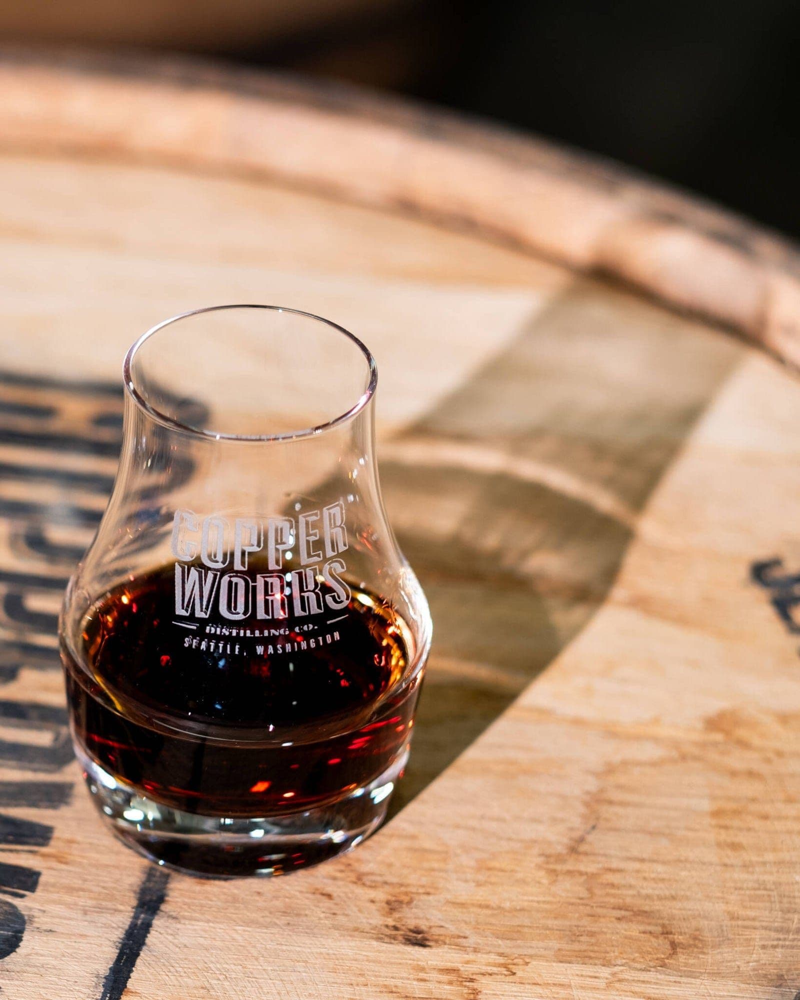 A Copperworks tasting glass of whiskey resting on the head of a cask.