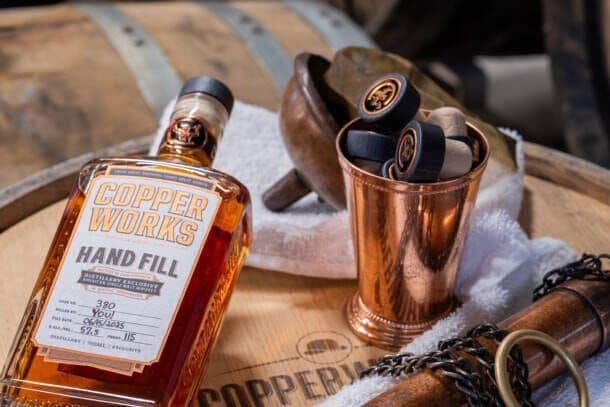 A Copperworks Hand Fill whiskey bottle beside a copper dipping dog on top of a cask.