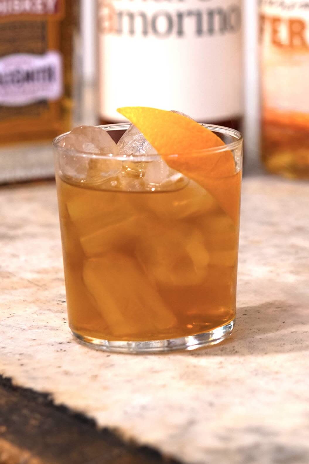A Mezzo e Mezzo on ice with an orange peel, in front of bottles of Maltsmith and Amaro Amorino
