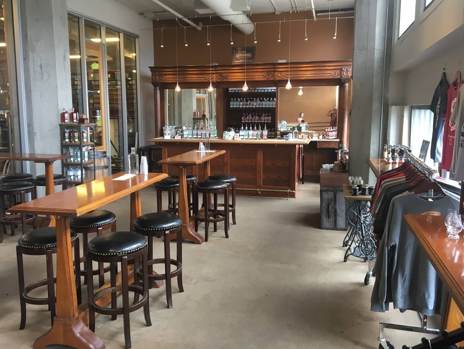The Seattle tasting room: a carved antique wooden bar, high-top tables with leather stools, and Copperworks apparel by the windows