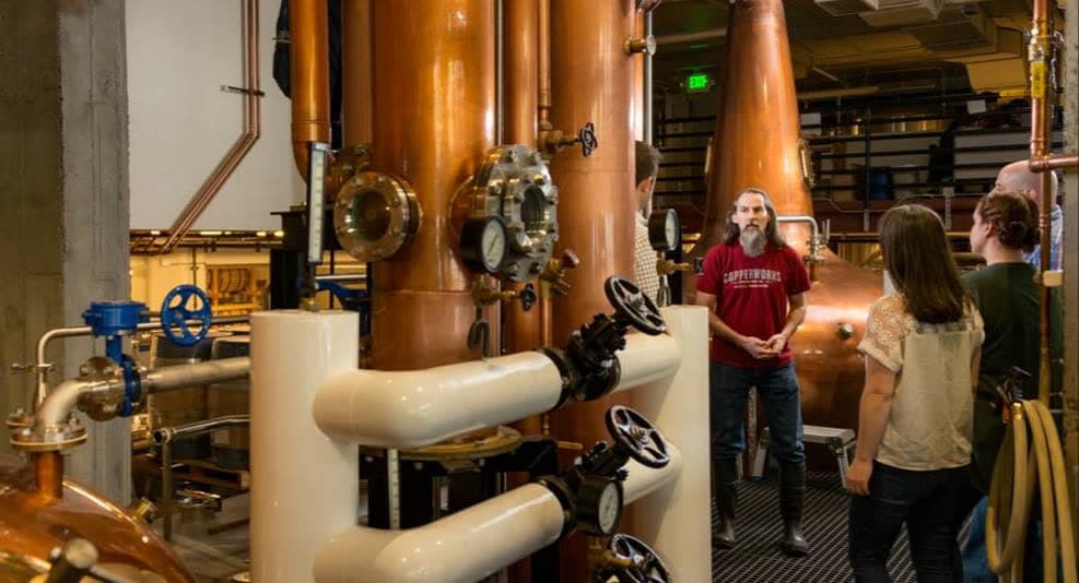 A Copperworks guide talks with a small tour group among the copper stills and pipework of the Seattle distillery